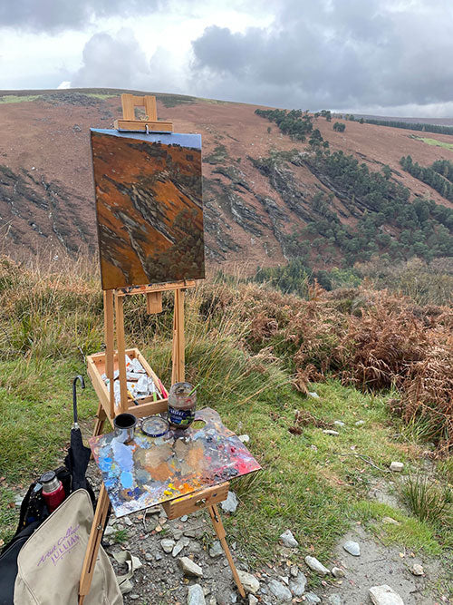 A painting in progress on an easel on location in Glendalough, the view is of a valley wall in the disctance.